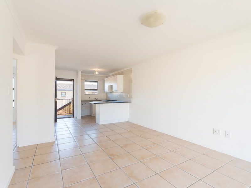 An open-plan living and kitchen area featuring neutral tiled flooring, white cabinetry, and a functional kitchen layout with built-in appliances.