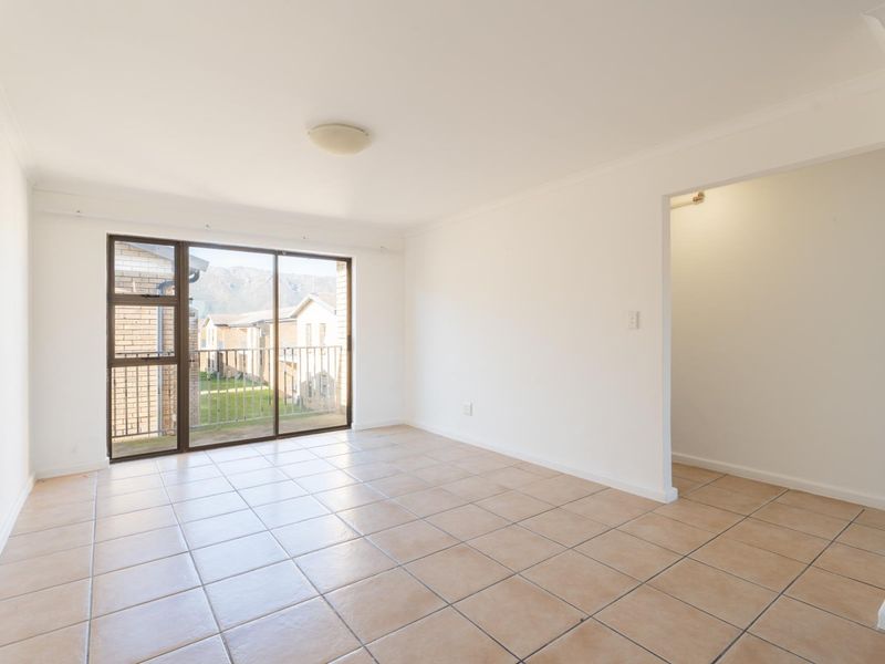 A bright, empty living room featuring neutral tiled flooring and a large sliding glass door providing access to a balcony.
