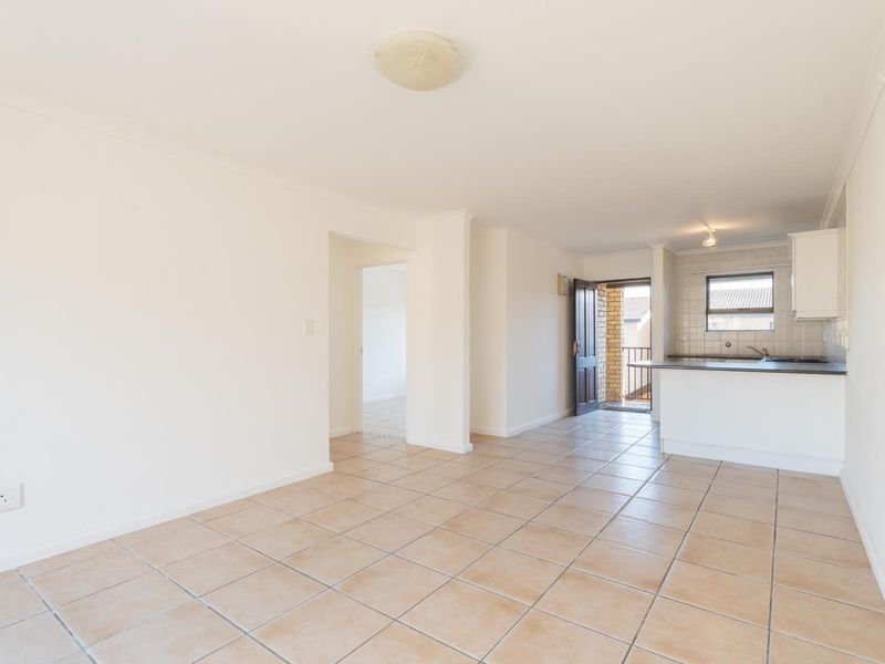 An open-plan living and kitchen area featuring neutral tiled flooring, built-in kitchen cabinetry with a countertop, and direct access to an exterior balcony.