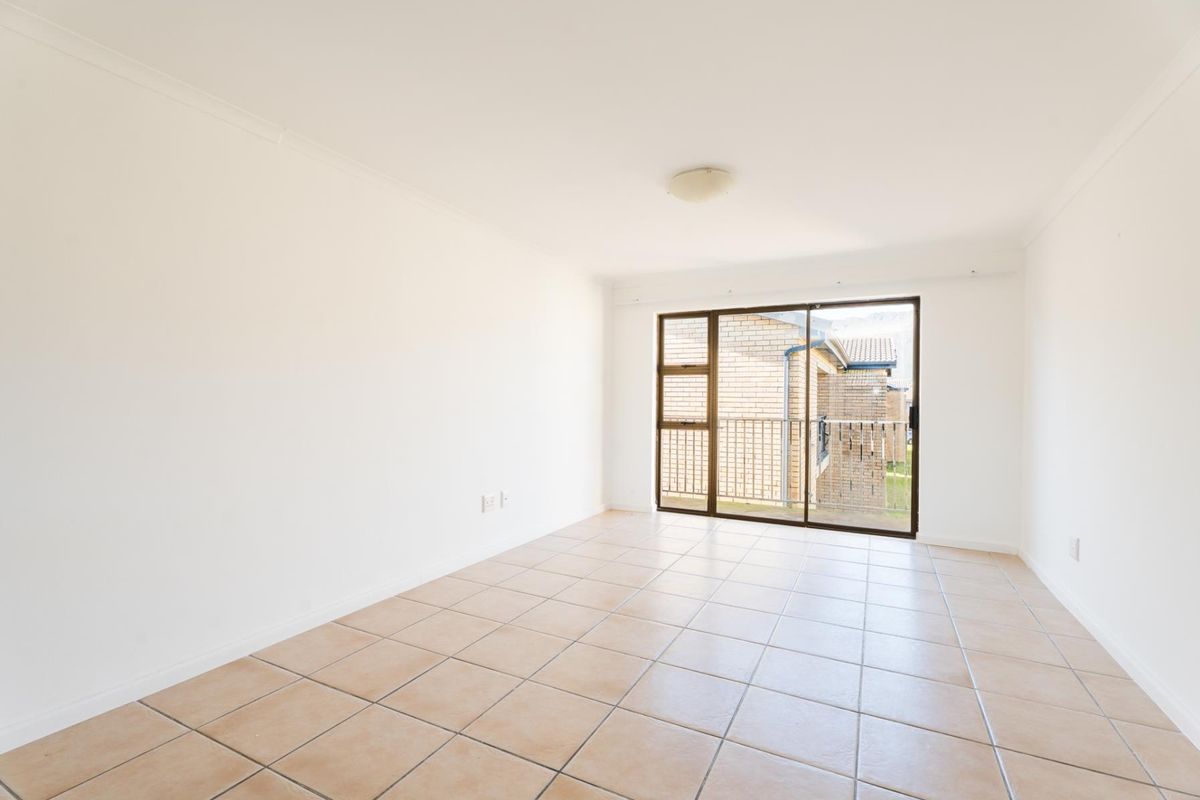 A bright, empty living room featuring neutral tiled flooring and a large sliding glass door providing access to an outdoor balcony area.
