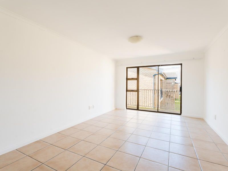 A bright, empty living room featuring neutral tiled flooring and a large sliding glass door providing access to an outdoor balcony area.