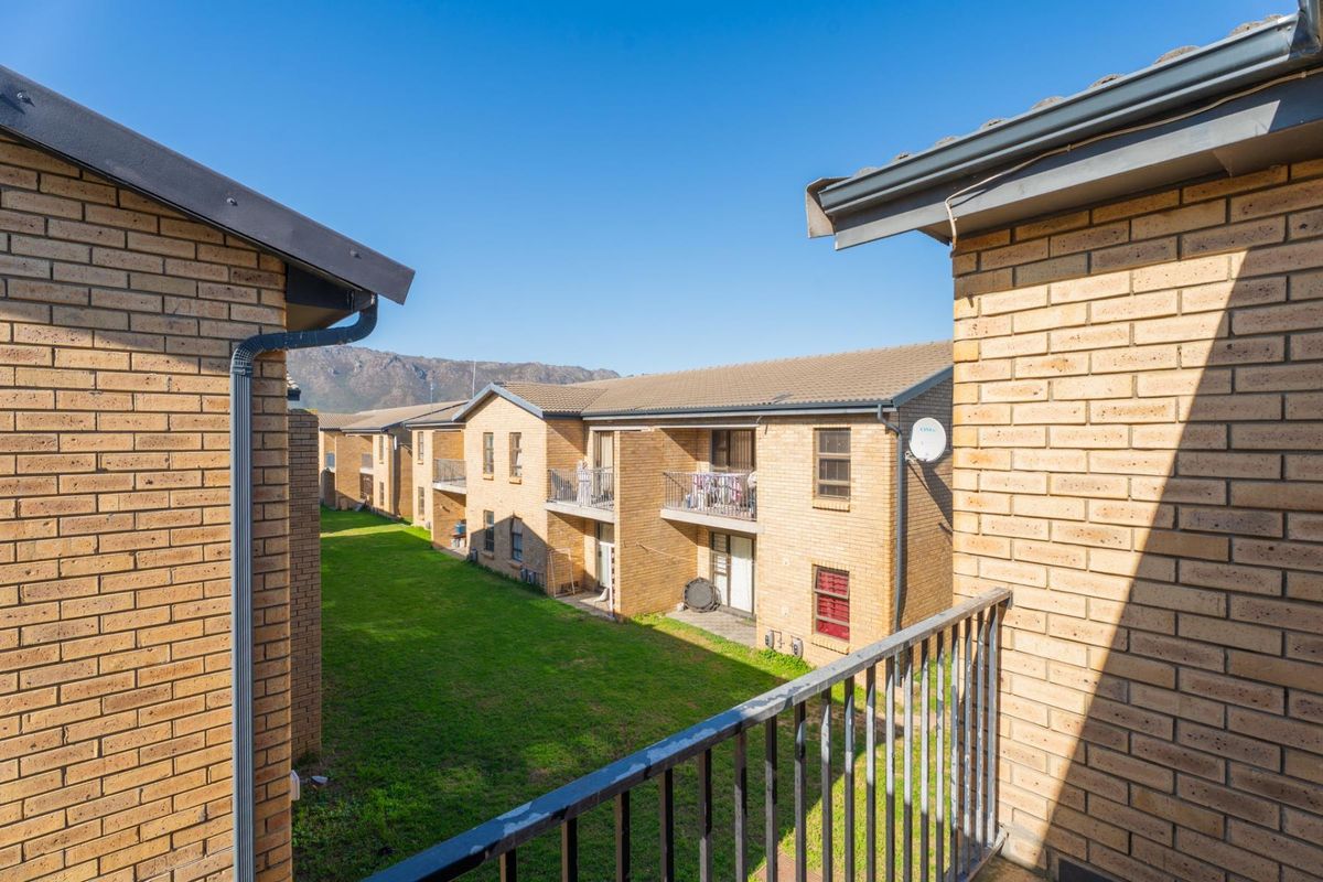 View of the apartment complex rear elevation featuring face brick facades, communal lawn area, and balcony structures.