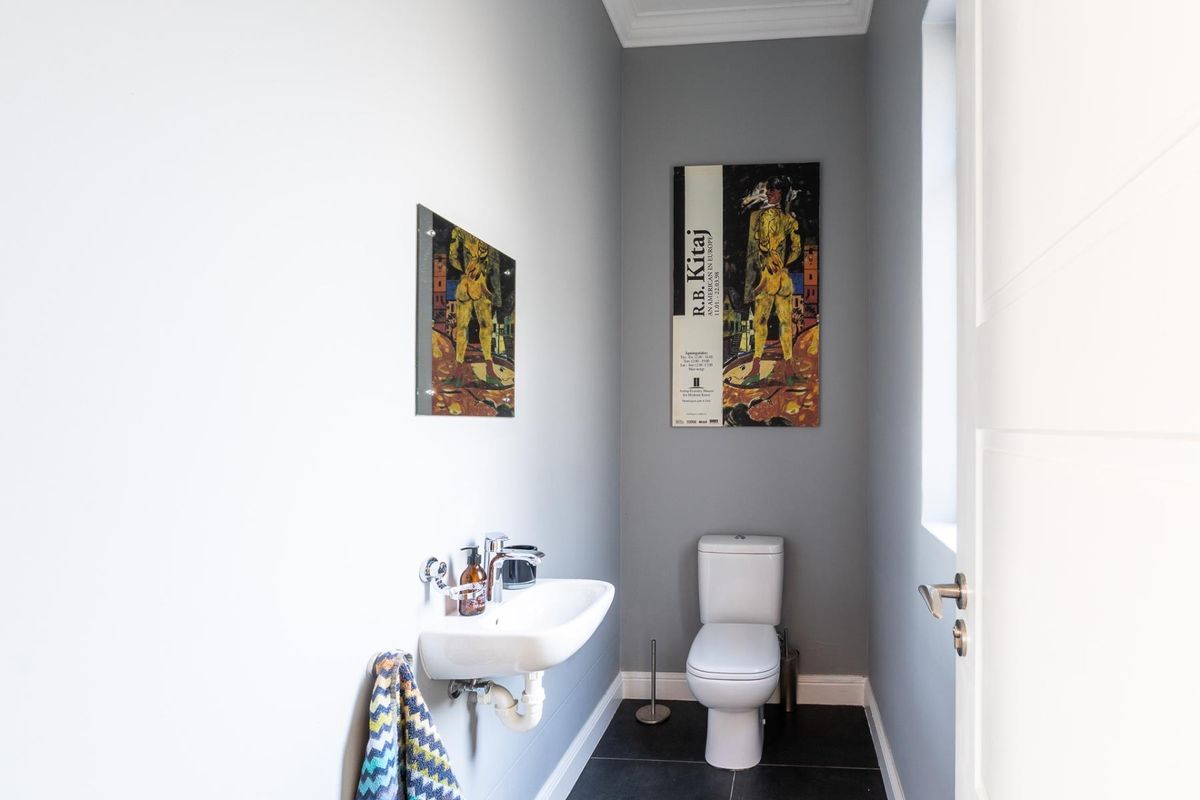 A compact guest cloakroom featuring a wall-mounted basin and a modern toilet with dark floor tiling and neutral grey walls.