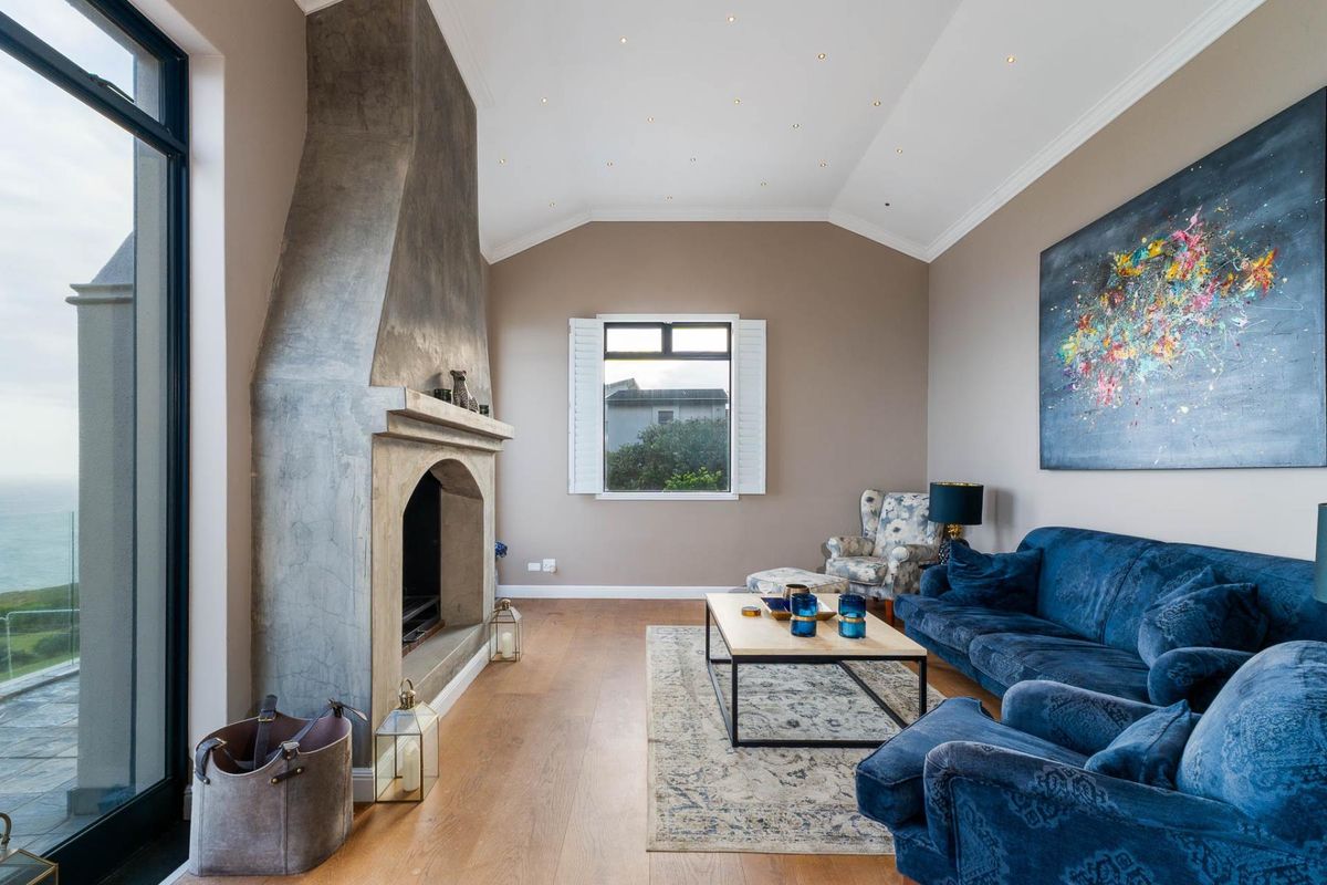 Spacious living room featuring a striking floor-to-ceiling concrete fireplace, vaulted ceilings with recessed lighting, and large glass doors opening to a scenic view.