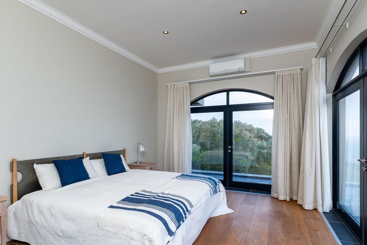 Spacious bedroom featuring hardwood flooring, recessed lighting, crown molding, and large arched glass doors providing access to an outdoor balcony with scenic views.