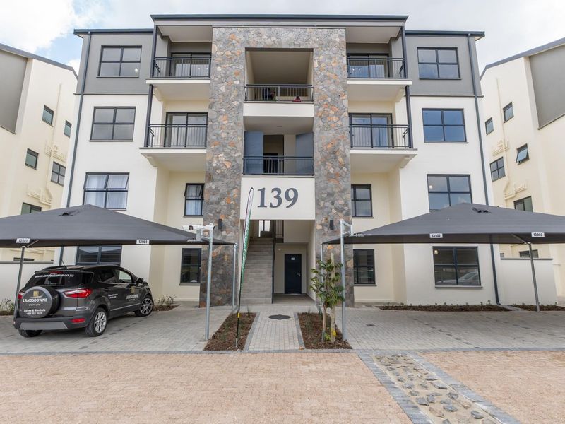 Front elevation of a modern multi-story apartment building featuring stone facade accents, private balconies, and dedicated covered parking bays.
