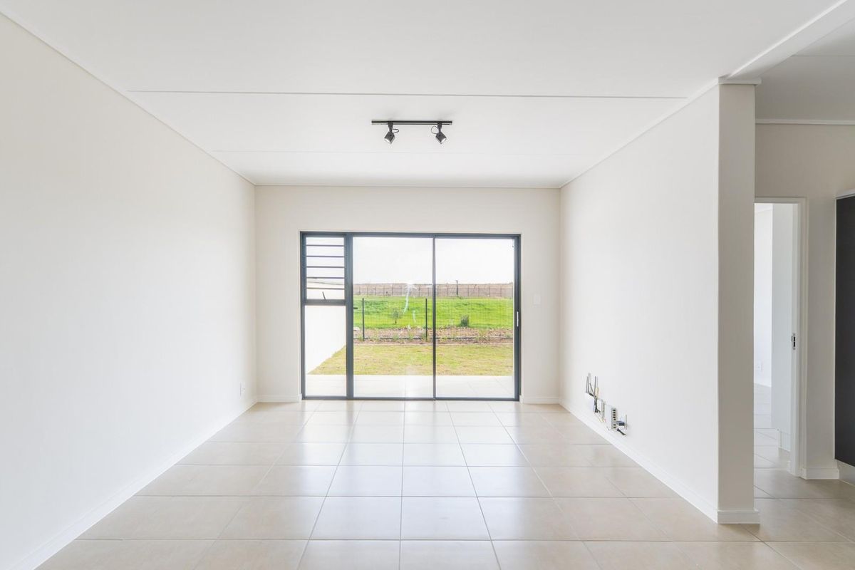 A bright, open-plan living area featuring neutral tiled flooring, modern track lighting, and a large sliding glass door providing access to the rear garden.