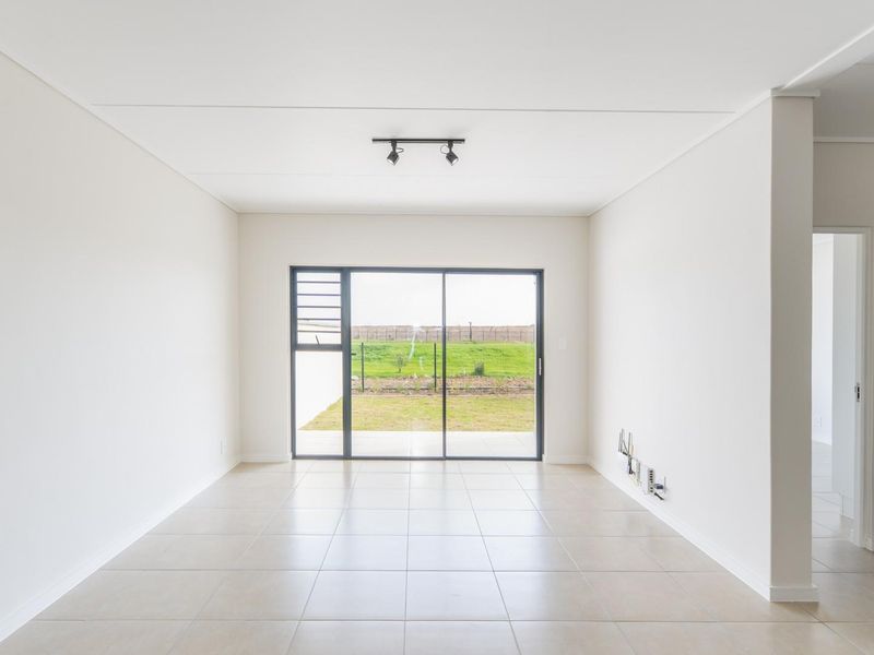 A bright, open-plan living area featuring neutral tiled flooring, modern track lighting, and a large sliding glass door providing access to the rear garden.