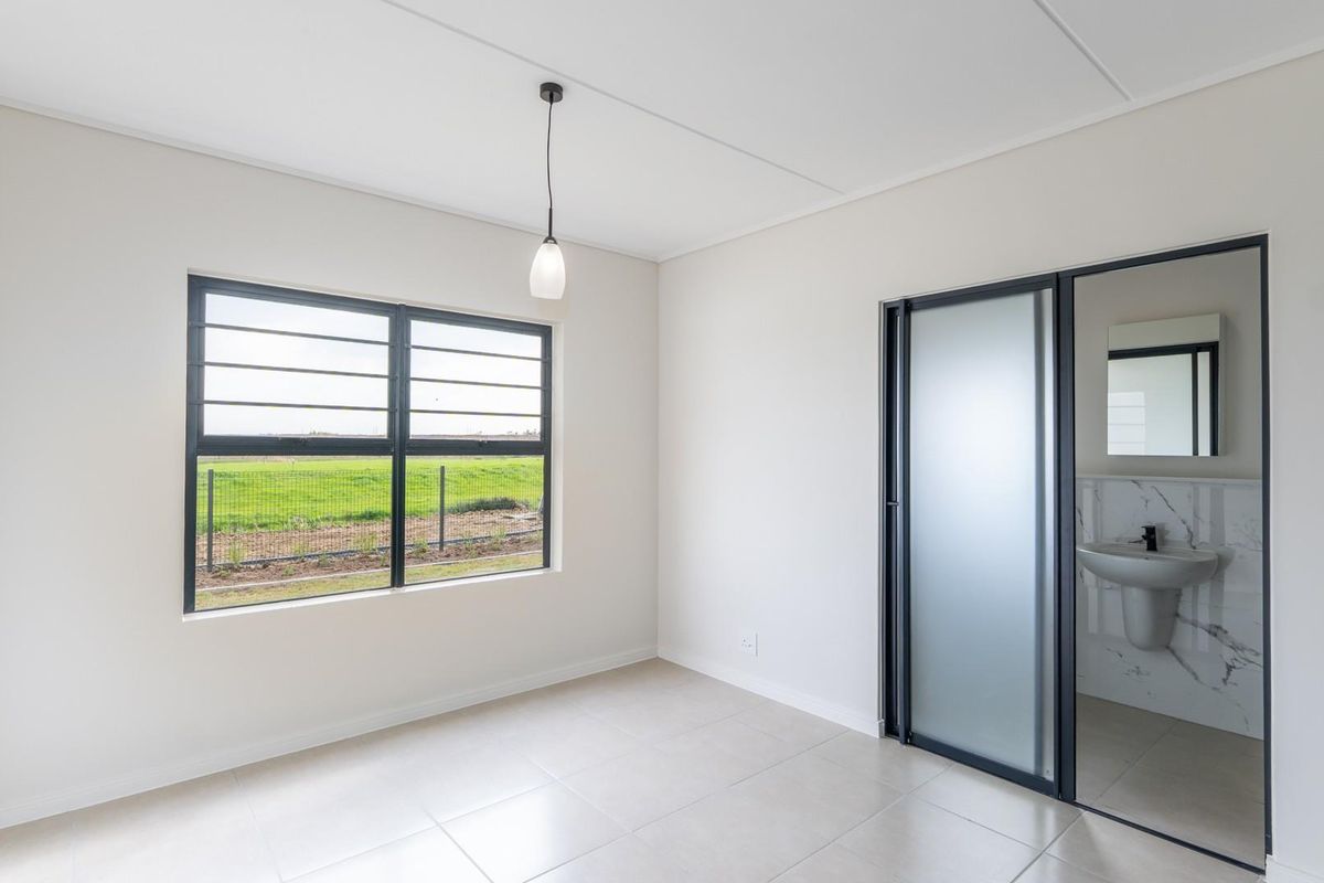 A bright, modern bedroom featuring neutral tiled flooring, large windows with security bars, and an en-suite bathroom with a sleek pedestal basin.