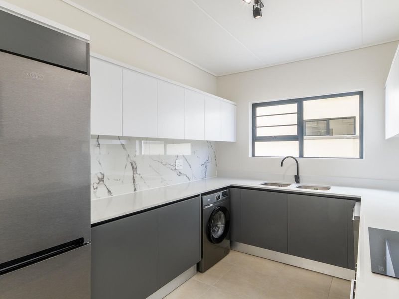 Modern kitchen featuring sleek grey and white cabinetry, marble-look splashback, quartz countertops, and integrated appliances including a hob and washing machine.