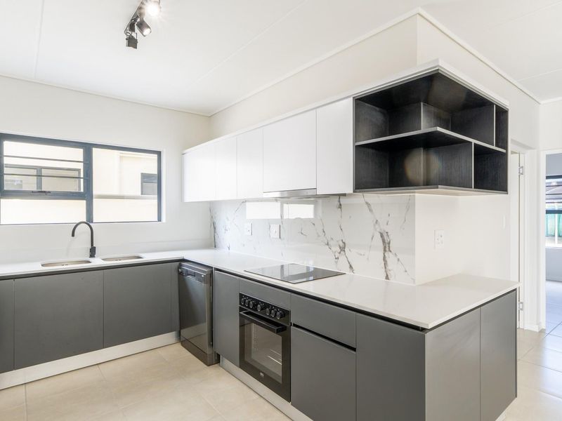 Modern kitchen featuring sleek grey and white cabinetry, marble-look splashback, built-in oven, electric hob, and double sink with contemporary fixtures.