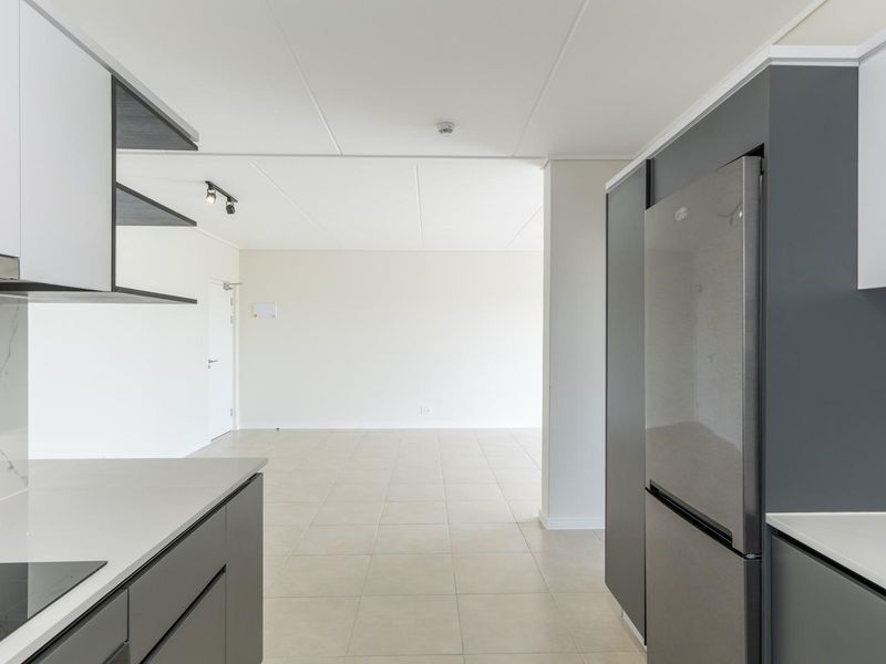 Modern open-plan kitchen featuring sleek grey and white cabinetry, stone countertops, and integrated appliances, flowing into a spacious, tiled living area.