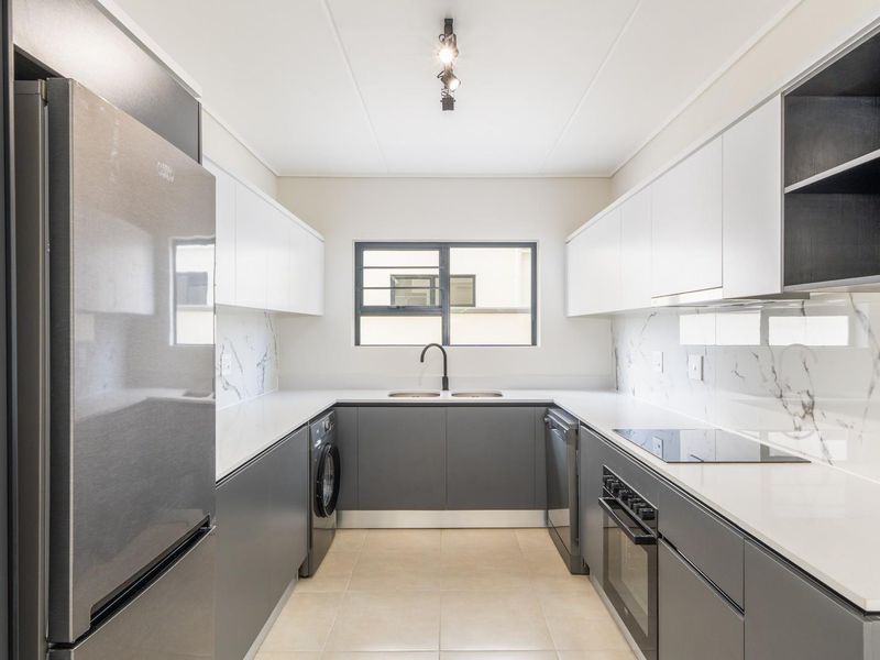 Modern galley-style kitchen featuring sleek two-tone cabinetry, stone countertops, marble-look splashbacks, and integrated appliances including an oven, hob, and laundry connection.