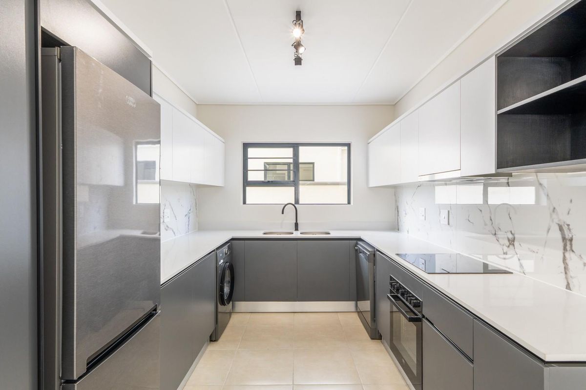 Modern galley-style kitchen featuring sleek two-tone cabinetry, stone countertops, marble-look splashbacks, and integrated appliances including an oven, hob, and laundry connection.