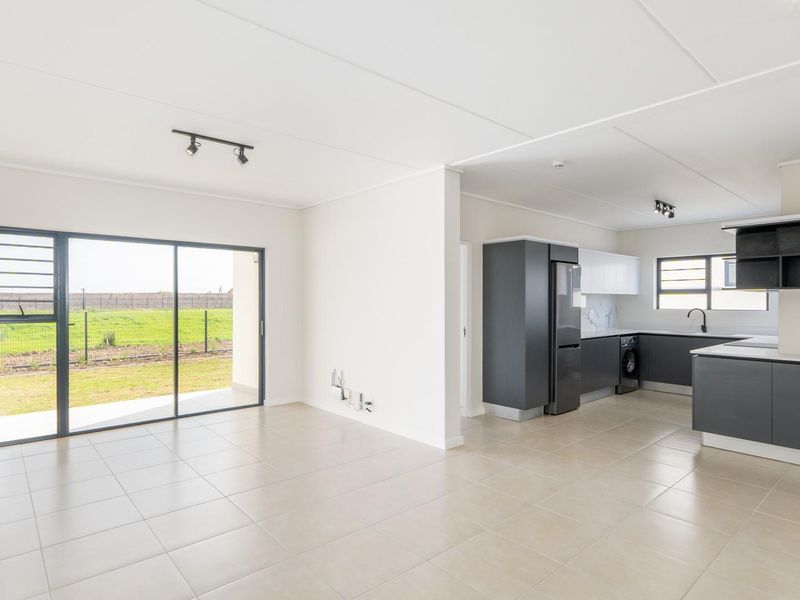 Modern open-plan living area featuring tiled floors, track lighting, and a sleek kitchen with built-in cabinetry, leading to an outdoor patio area.