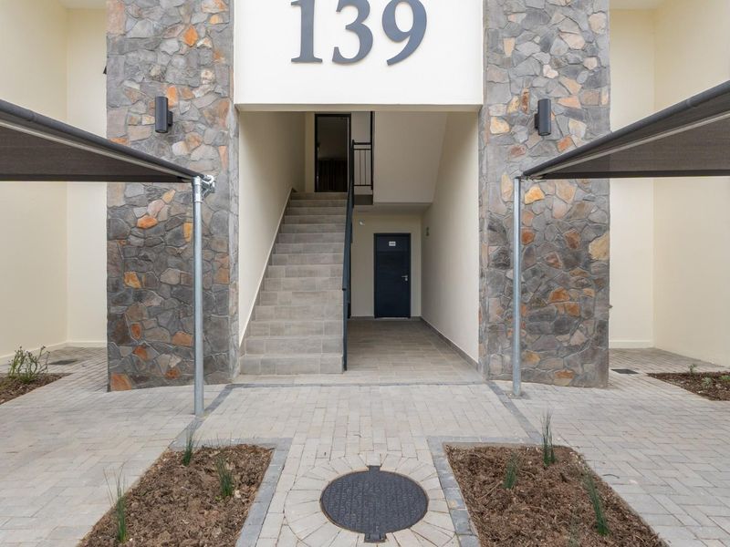Front entrance of the apartment building featuring stone cladding, paved driveway, and modern shade sails over parking areas.