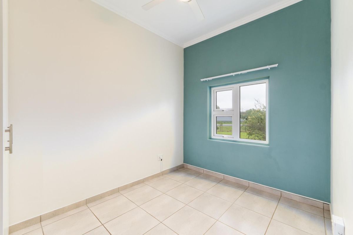 A bright, empty bedroom featuring neutral tiled flooring, a ceiling fan, and a feature wall with a window.