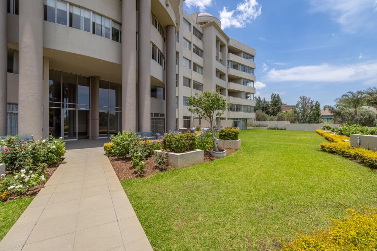 A well-maintained exterior view of the apartment building featuring a paved walkway, landscaped garden beds, and a manicured lawn area.