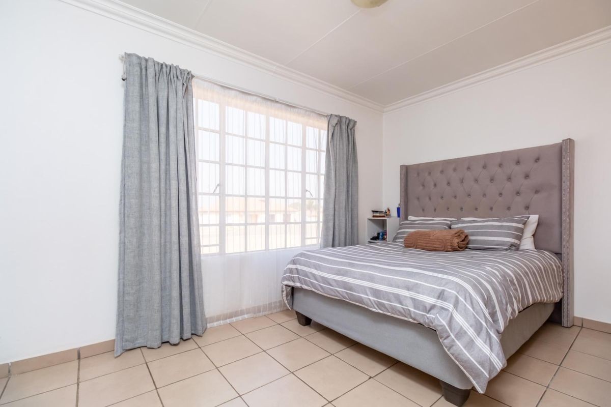 A well-lit bedroom featuring neutral tiled flooring, large window with curtain tracks, and crown molding.