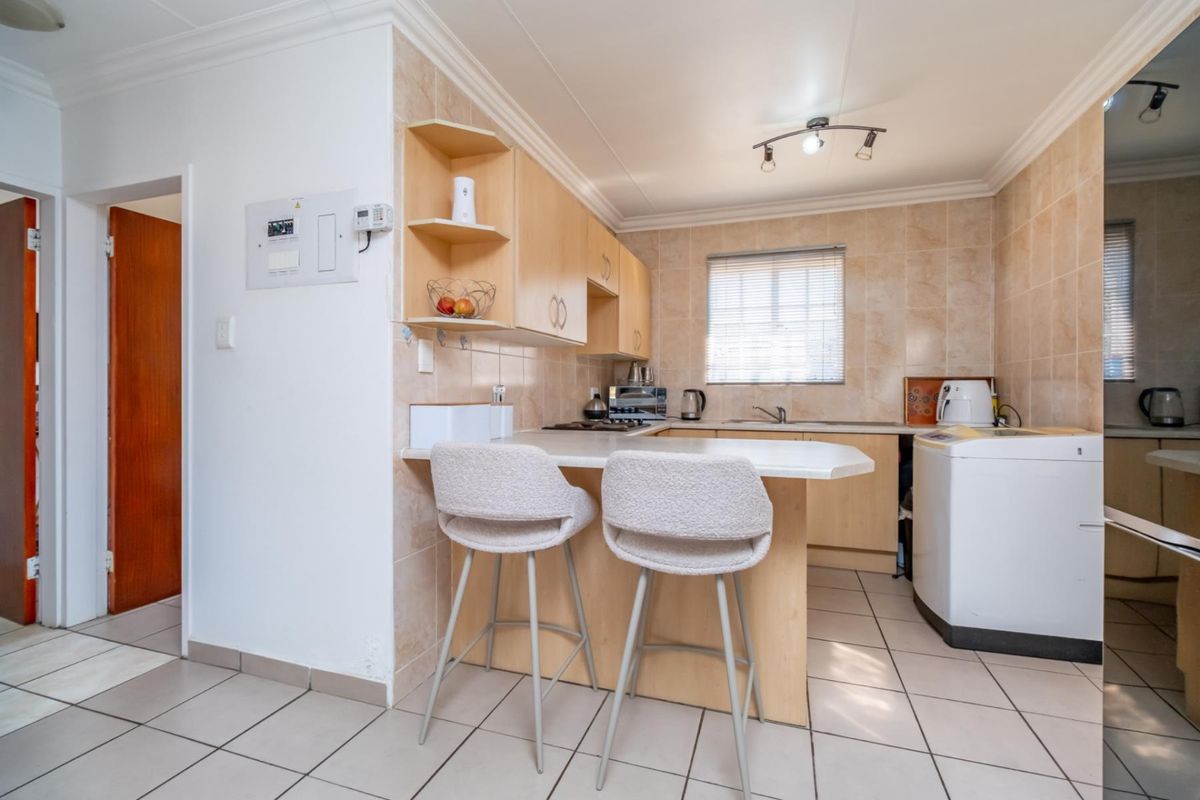 Functional kitchen featuring light wood cabinetry, tiled splashbacks, a breakfast bar, and integrated laundry space with tiled flooring.