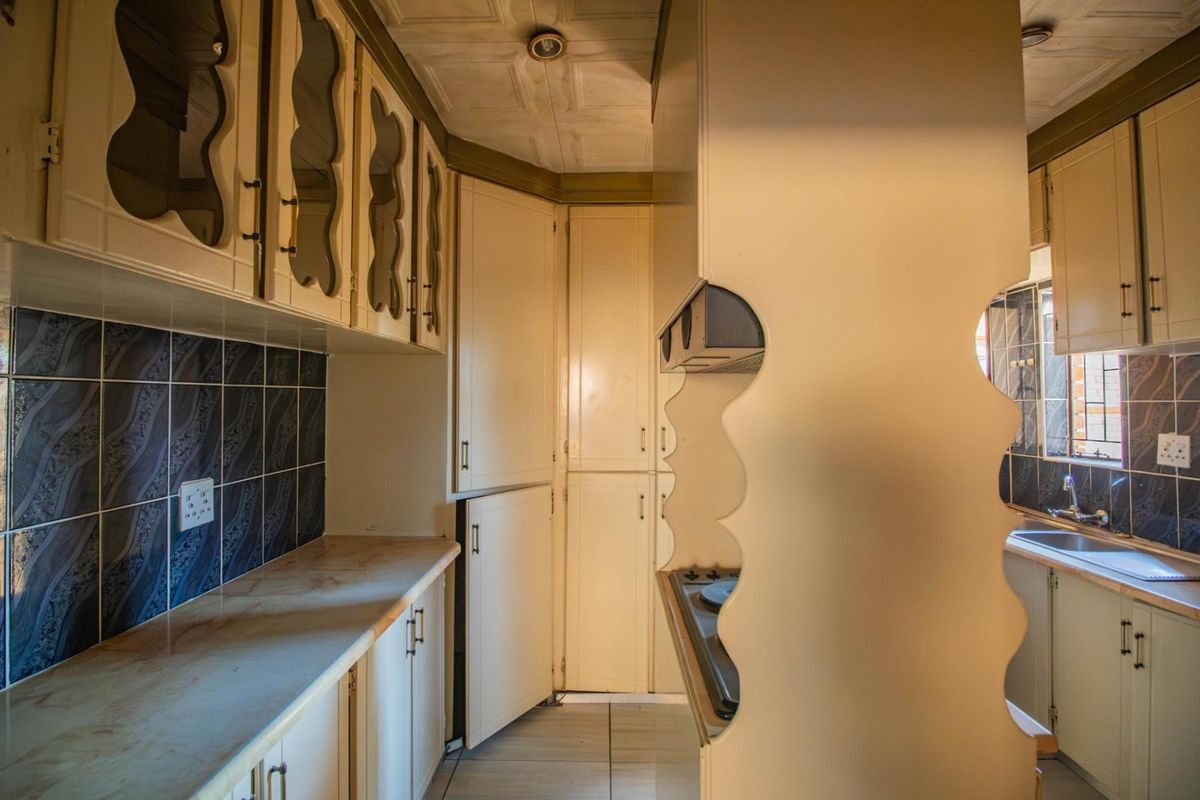 A functional kitchen featuring built-in cabinetry, a tiled splashback, integrated hob, and a stainless steel sink with ample storage space.