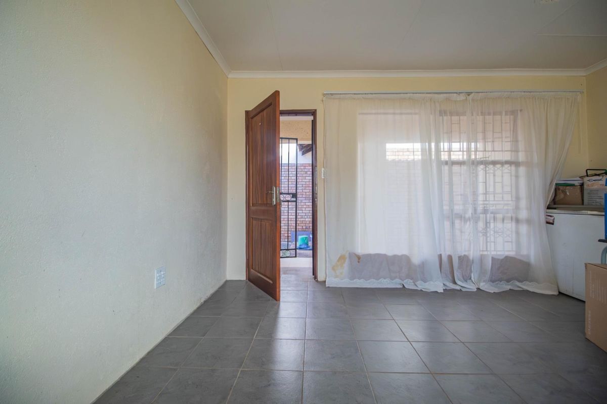 A functional living area featuring tiled flooring, a wooden door leading to an exterior space, and large windows with curtains.
