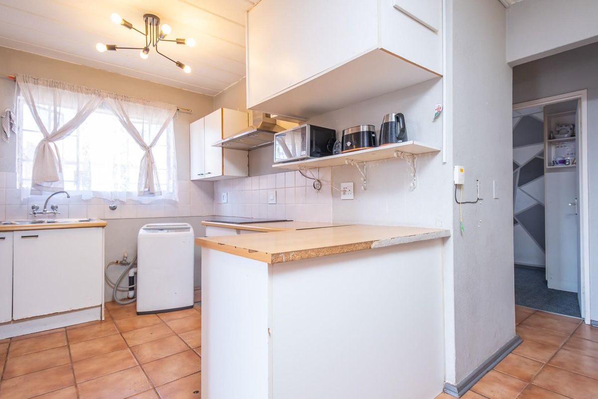 A functional kitchen featuring white cabinetry, tiled flooring, a built-in extractor fan, and a breakfast counter, offering a practical layout for daily use.