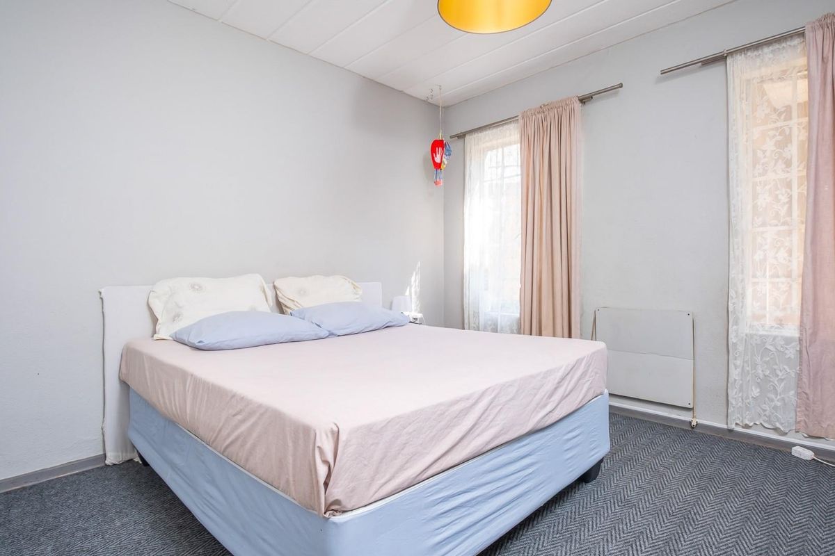 A functional bedroom featuring carpeted flooring, dual windows with curtain rods, and a wall-mounted heater.