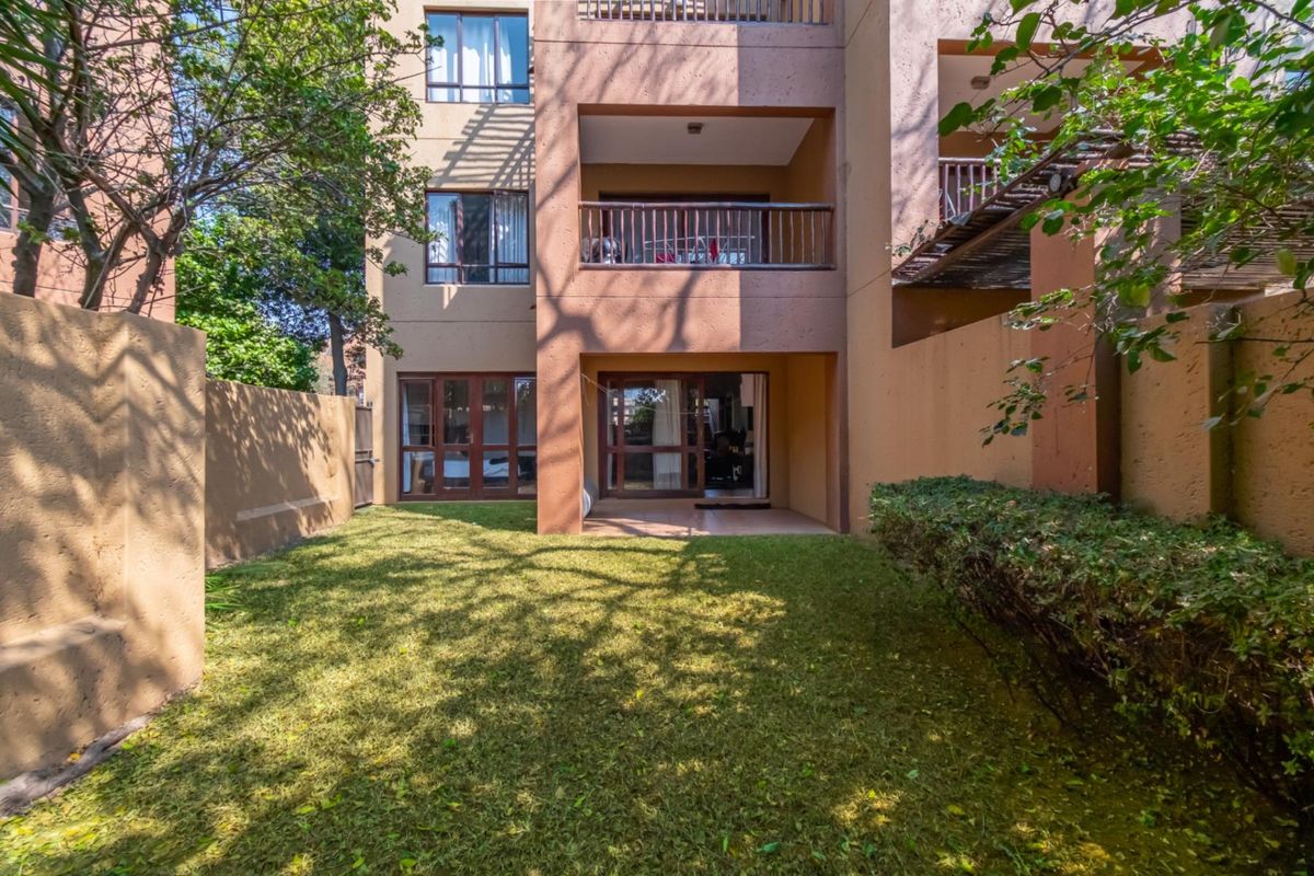 A rear view of the apartment building featuring a private garden area, ground floor patio, and upper-level balconies with wooden railings.