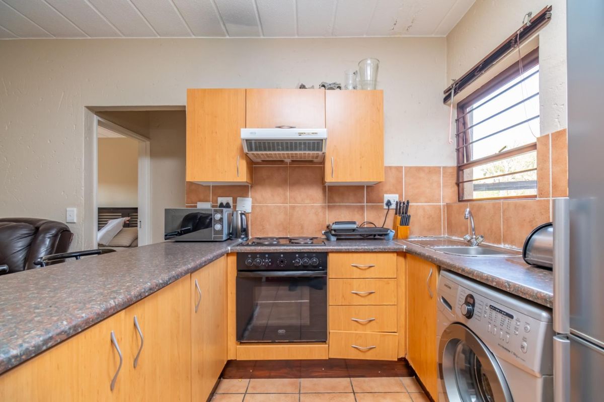 A functional kitchen featuring light wood cabinetry, tiled backsplash, built-in oven, hob, extractor fan, and integrated laundry plumbing.