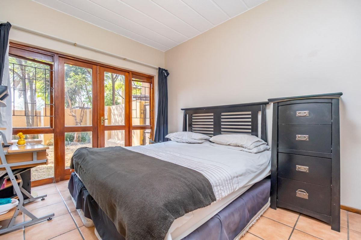 A bedroom featuring tiled flooring and large wooden-framed glass doors providing direct access to the outdoor area.