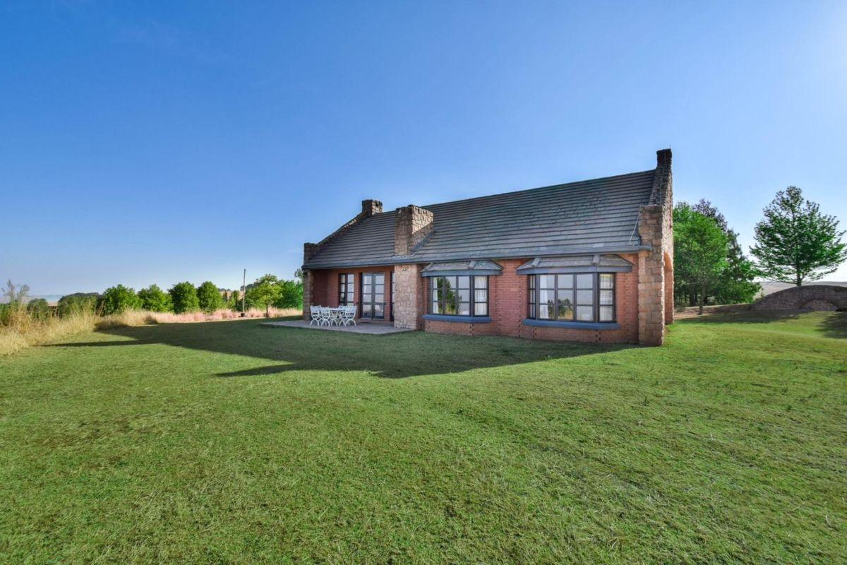 Rear view of a charming brick and stone house featuring bay windows, french doors, and a paved patio overlooking a spacious lawn.