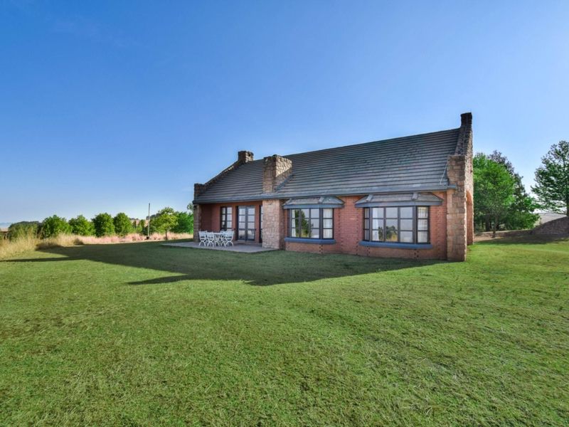 Rear view of a charming brick and stone house featuring bay windows, french doors, and a paved patio overlooking a spacious lawn.