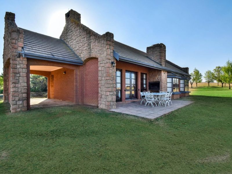 Rear view of a charming brick and stone house featuring a covered patio, paved outdoor entertainment area, and expansive garden views.