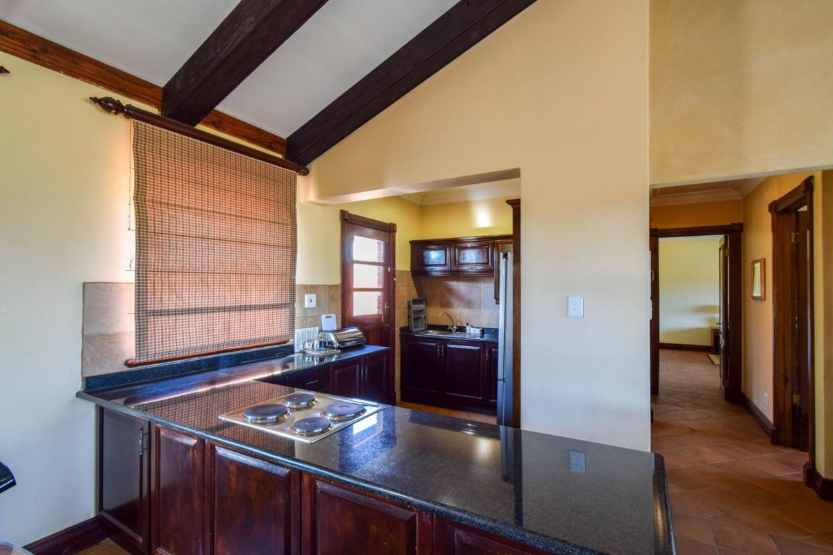 Kitchen featuring dark wood cabinetry, granite countertops, built-in hob, and exposed timber ceiling beams, with an adjacent scullery area and tiled flooring.