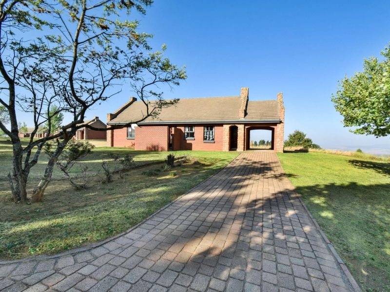 A charming single-story brick house featuring a tiled roof, a covered entrance, and a paved driveway set within a spacious, well-maintained garden.