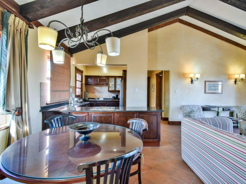 Spacious open-plan living and dining area featuring vaulted ceilings with exposed timber beams, terracotta flooring, and a functional kitchen with dark wood cabinetry.