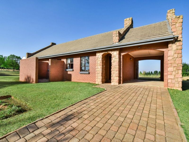 A well-maintained single-story brick house featuring stone accents, a tiled roof, and an integrated carport, set on a spacious landscaped lawn.