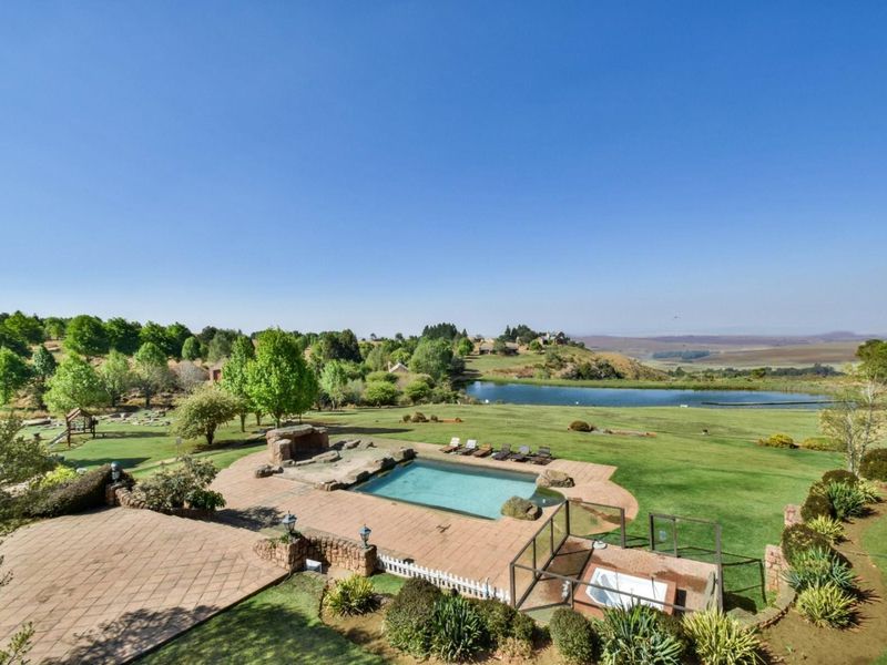 Expansive outdoor entertainment area featuring a swimming pool, hot tub, built-in stone fireplace, and paved patio overlooking a scenic landscape and lake.