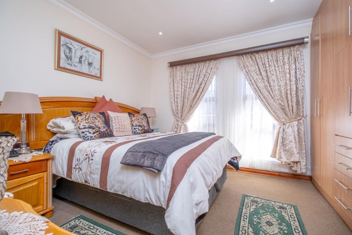A well-maintained bedroom featuring built-in wooden cupboards, carpeted flooring, and large windows with curtain treatments.