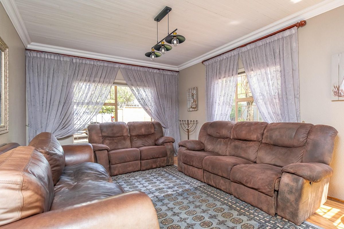 A comfortable living room featuring timber-look flooring, crown molding, and large windows with curtains, providing a bright and inviting space for relaxation.