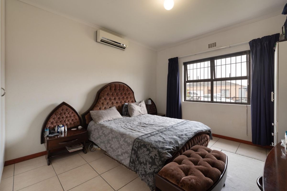 A bedroom featuring tiled flooring, a wall-mounted split-system air conditioner, and a window fitted with security bars.