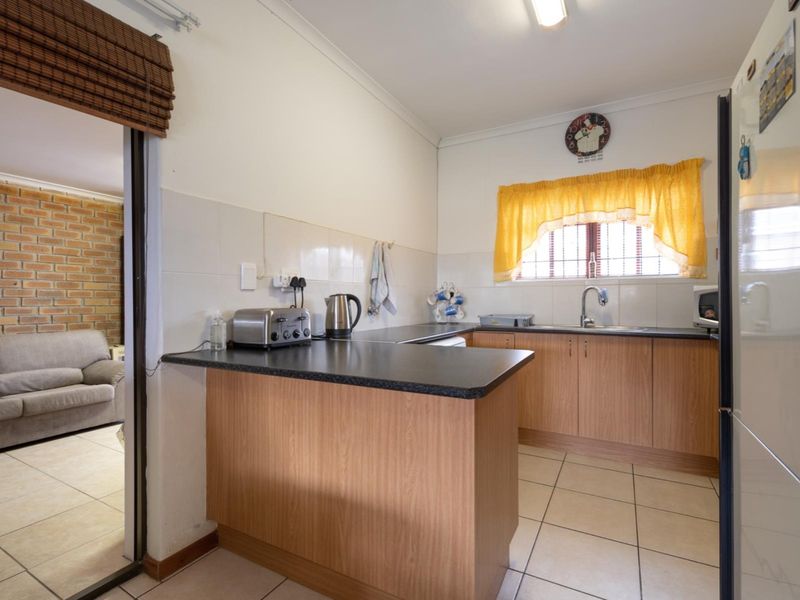 A functional kitchen featuring laminate cabinetry, dark countertops, tiled splashbacks, and ceramic floor tiles, with an open-plan layout connecting to the living area.