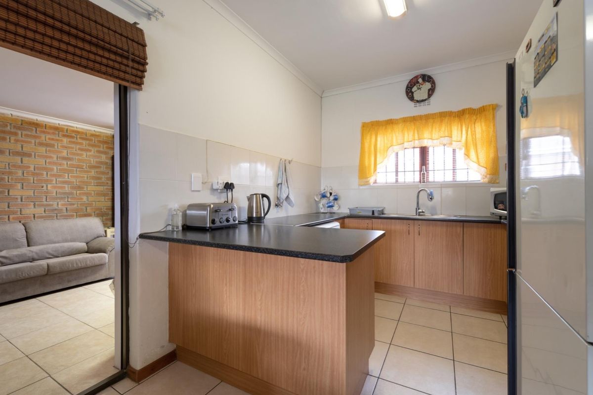 A functional kitchen featuring laminate cabinetry, dark countertops, tiled splashbacks, and ceramic floor tiles, with an open-plan layout connecting to the living area.