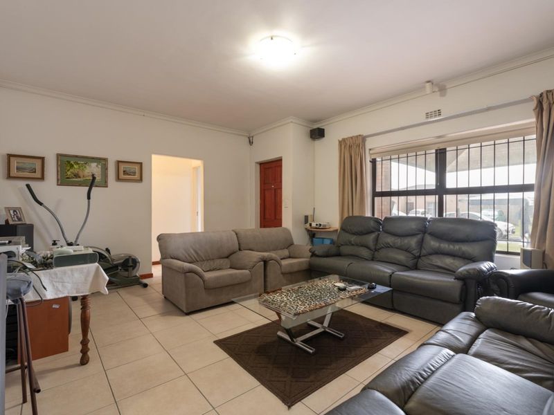 A spacious living room featuring tiled flooring, large windows with security bars, and neutral wall finishes.