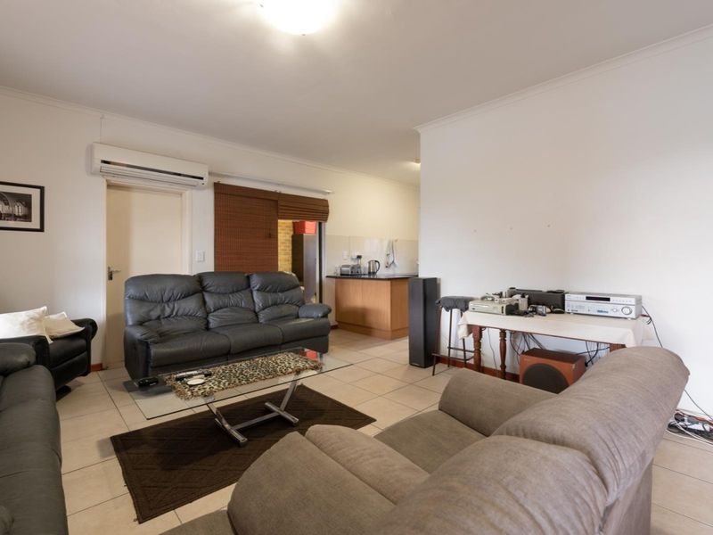 Open-plan living area featuring tiled flooring, a wall-mounted air conditioning unit, and a functional kitchen space with built-in cabinetry.