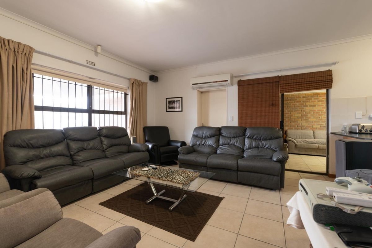 Spacious living room featuring tiled flooring, a wall-mounted split-system air conditioner, and large windows with security bars.