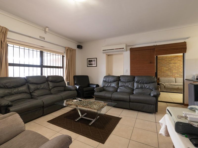 Spacious living room featuring tiled flooring, a wall-mounted split-system air conditioner, and large windows with security bars.