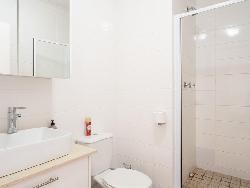 A clean, functional bathroom featuring a modern vessel sink, vanity cabinet, toilet, and a glass-enclosed shower with tiled finishes.