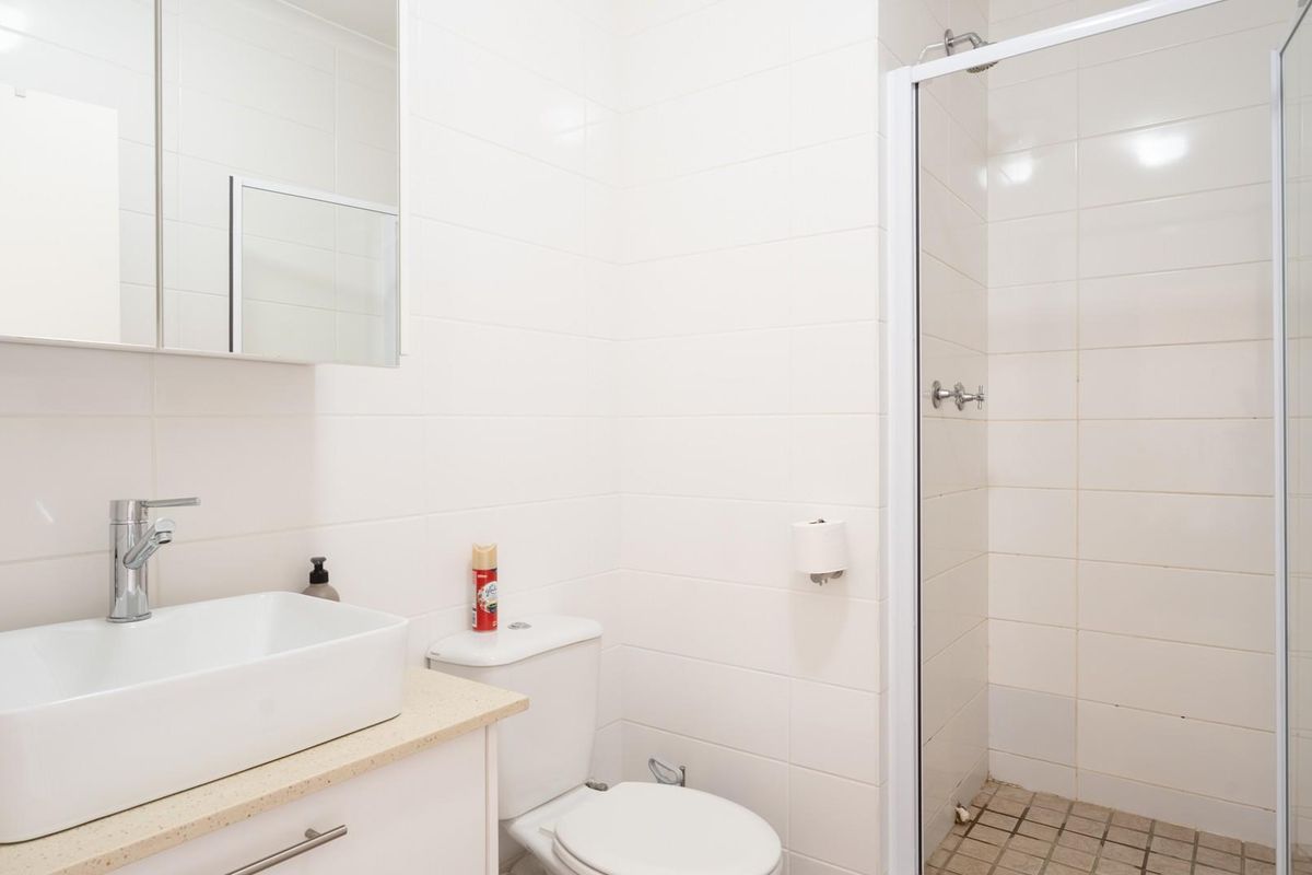 A clean, functional bathroom featuring a modern vessel sink, vanity cabinet, toilet, and a glass-enclosed shower with tiled finishes.